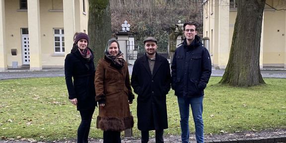 Dok-Seminar AIG-Cluster 2023 Zwei Frauen und zwei Männer in Winterjacken stehen nebeneinander und schauen in Richtung Kamera. Im Hintergrund Wiese, zwei Bäume und Gebäude.