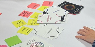 Flyer, Klebezettel und weitere Arbeitsmaterialien liegen auf Flipchart-Papier ausgebreitet auf einem Tisch.